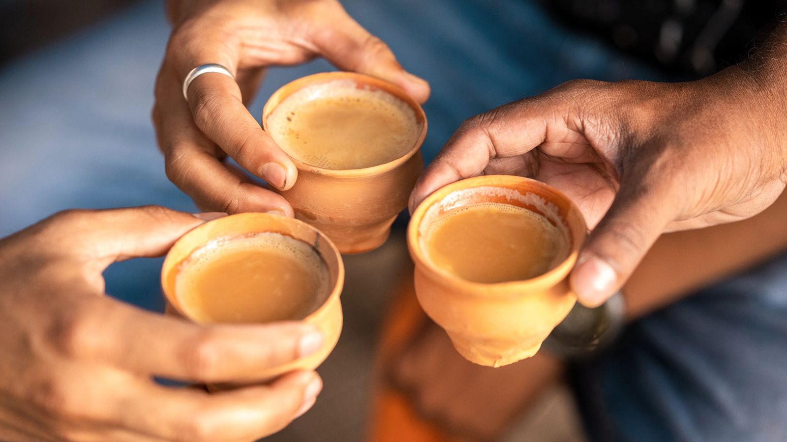 Three hands raising clay cups of Indian chai