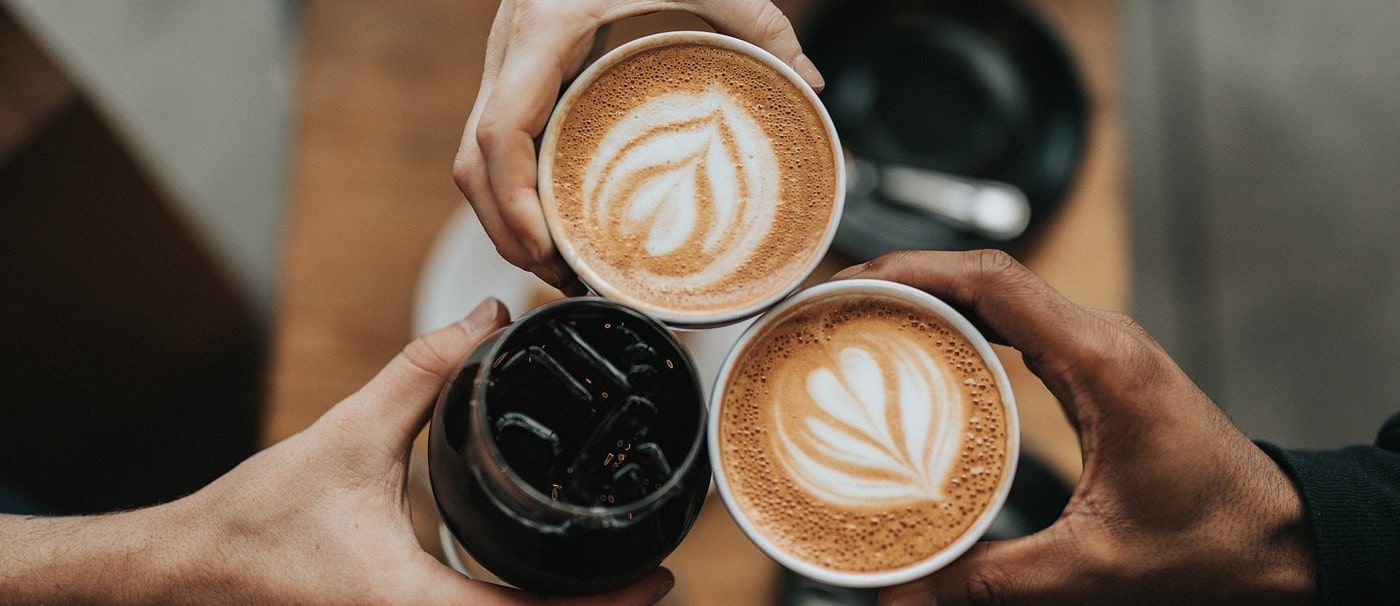 Three hands raising coffee cups together over a table