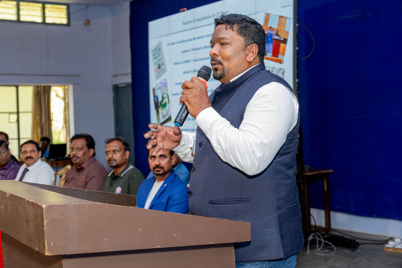 Venkatesh Kumar Pandurengan speaking with a microphone in front of a presentation screen